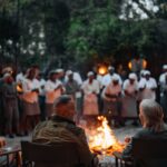 Guests enjoying a boma dinner at Chitabe Camp, featuring a circular firepit, lantern-lit seating, and a vibrant cultural atmosphere under the African night sky