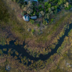 Drone shot of Mma Dinare Camp nestled beside winding river channels in the Okavango Delta.