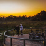 Guests standing on deck at sunset with fire pit at Mma Dinare Camp.