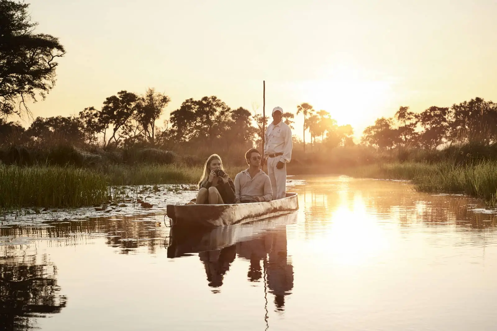 Botswana Honeymoon Safari: Private Water Camps & Moremi's Predators - Gallery Image 1 Couple on a private mokoro cruise through the Okavango Delta at sunset