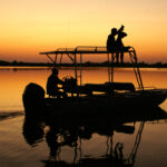 Safari boat at sunset on calm Okavango Delta waters near Kwara Camp.
