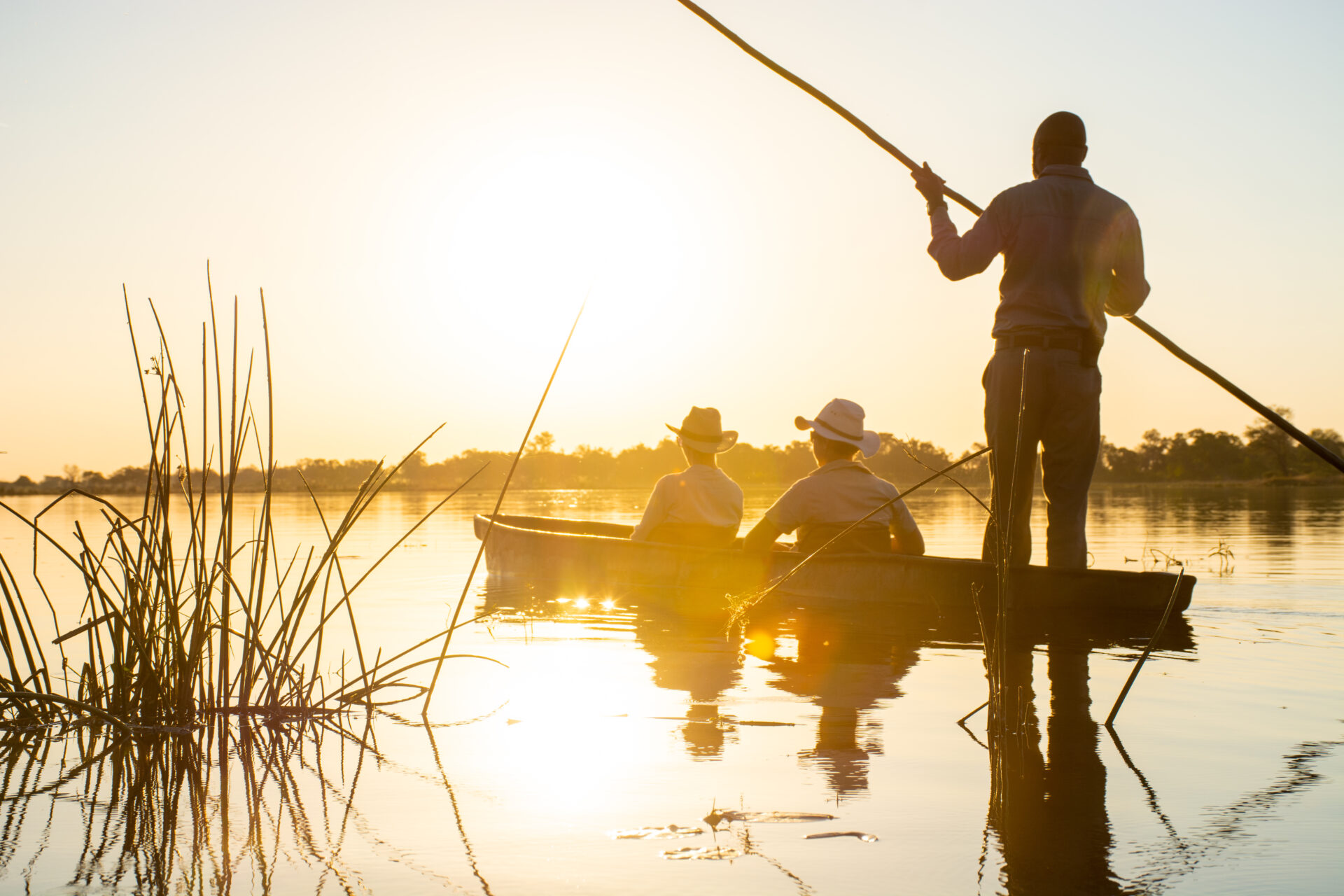 Guests in a mokoro canoe on the Okavango Delta during sunset at Kwara Camp.
