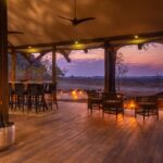 Outdoor lounge with bar and seating area overlooking sunset at Kwara Camp.
