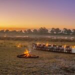 Outdoor dinner setup with campfire at sunset near Kwara Camp.