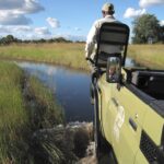 Safari guide driving through water in open 4x4 vehicle at Kwara Camp.