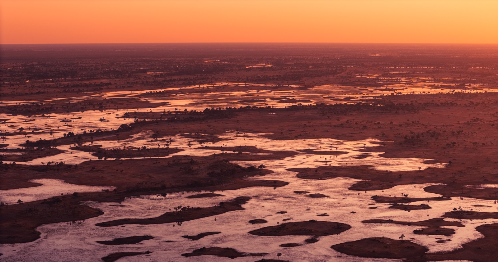 Sunset illuminating the winding waterways of Kanana Camp in the Okavango Delta, with reflections of the sky on the calm water surface.