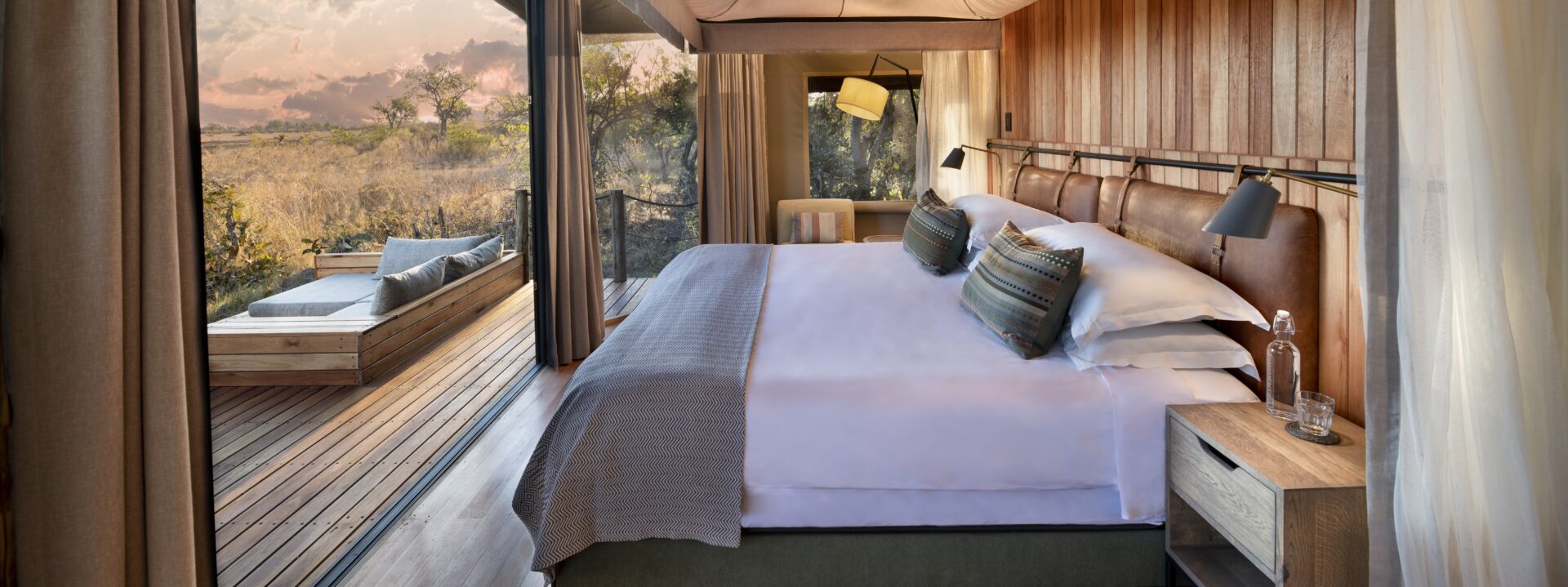 Spacious safari tent with a king-size bed, wooden interior, and sliding glass doors opening to a private deck overlooking the African bush.