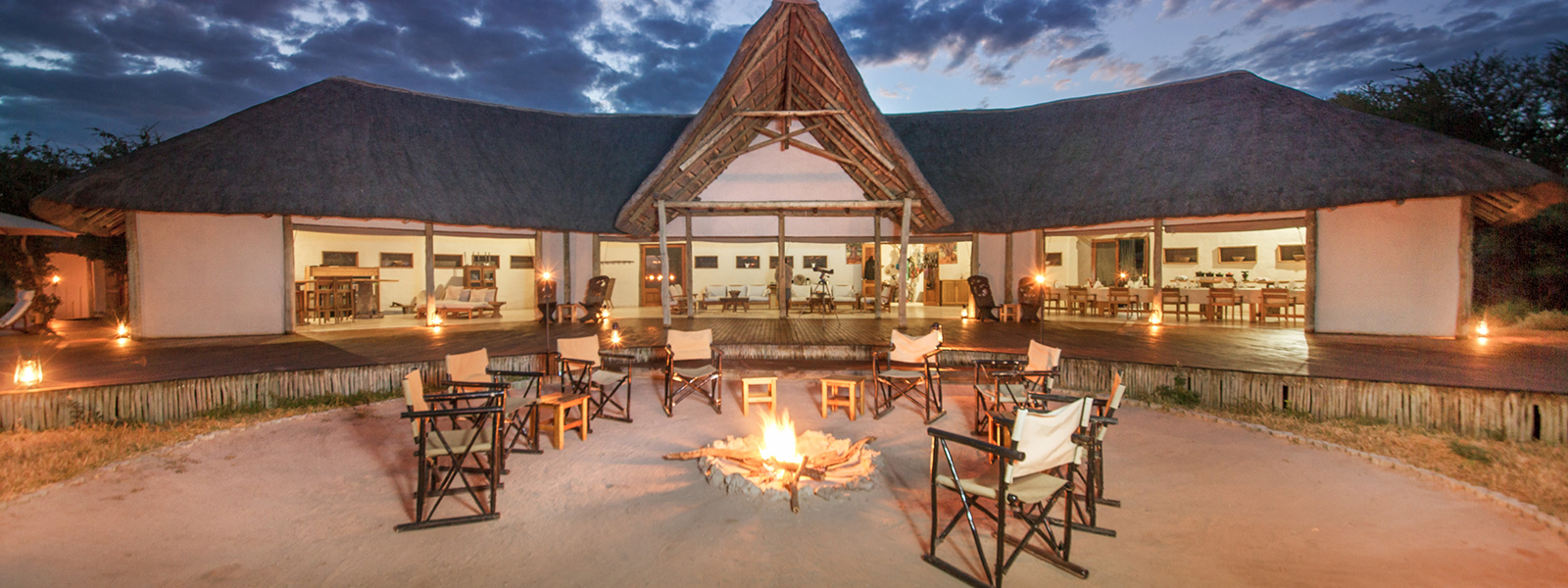 Thatched main lodge with open fire pit and seating area at Nxai Pan Camp.