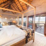 Spacious chalet bedroom with a four-poster bed and deck overlooking the Kalahari at Tau Pan Camp.