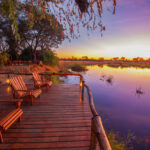 Wooden deck with chairs overlooking a calm river at sunset in Lagoon Camp.