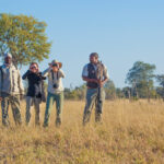 Group of safari guides and guests standing in grassy plains near Lagoon Camp.