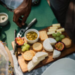 Cheese and cracker platter with grapes, olives, and passion fruit on a wooden board.