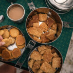 Hand reaching for biscuits beside a mug of tea on a green tablecloth.