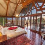 Elegant safari suite with wooden floors, large bed, and open glass walls overlooking the savanna.
