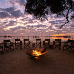 Firepit with chairs and sunset reflections over the lagoon at Pom Pom Camp.