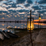 Lit lanterns and mokoro canoes beside the lagoon at sunset at Pom Pom Camp.