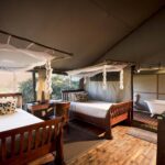 Twin tent bedroom interior at Khwai Ebony Camp with wooden floors and canopy beds.