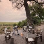 Khwai Ebony Camp campfire setup with chairs under a large tree in Botswana.