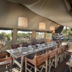 Linyanti Expeditions dining tent with long wooden table and safari decor in Botswana.