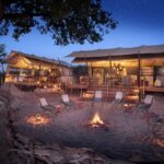 Linyanti Expeditions Camp firepit area with safari tents illuminated at night in Botswana.