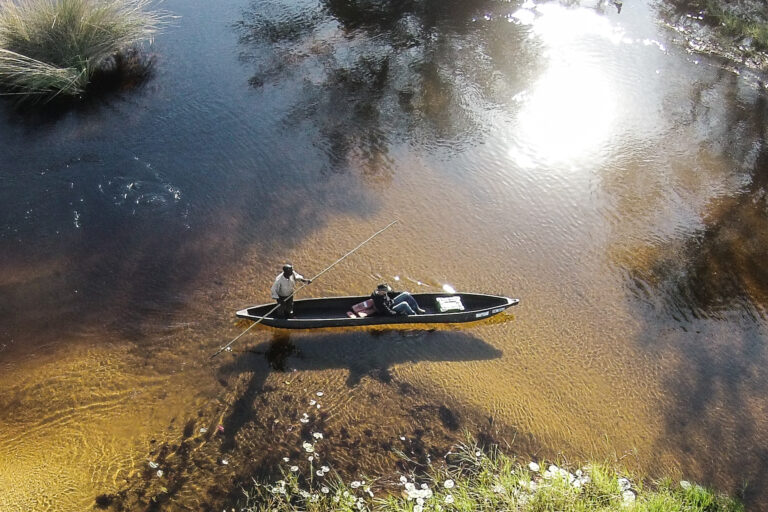 Two people in a mokoro canoe on shallow, clear water with reflections at Moremi Crossing in the Okavango Delta.