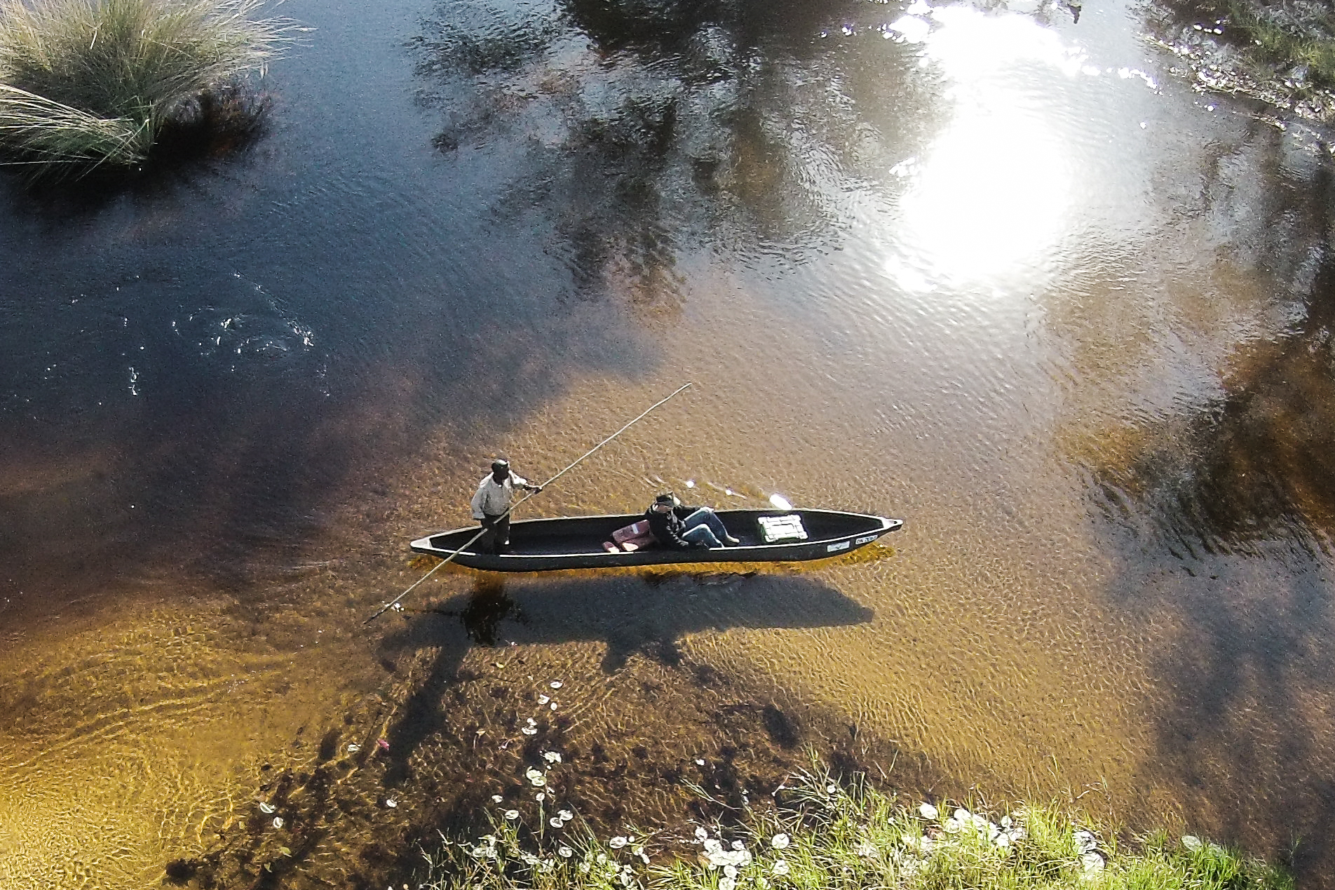 Two people in a mokoro canoe on shallow, clear water with reflections at Moremi Crossing in the Okavango Delta.