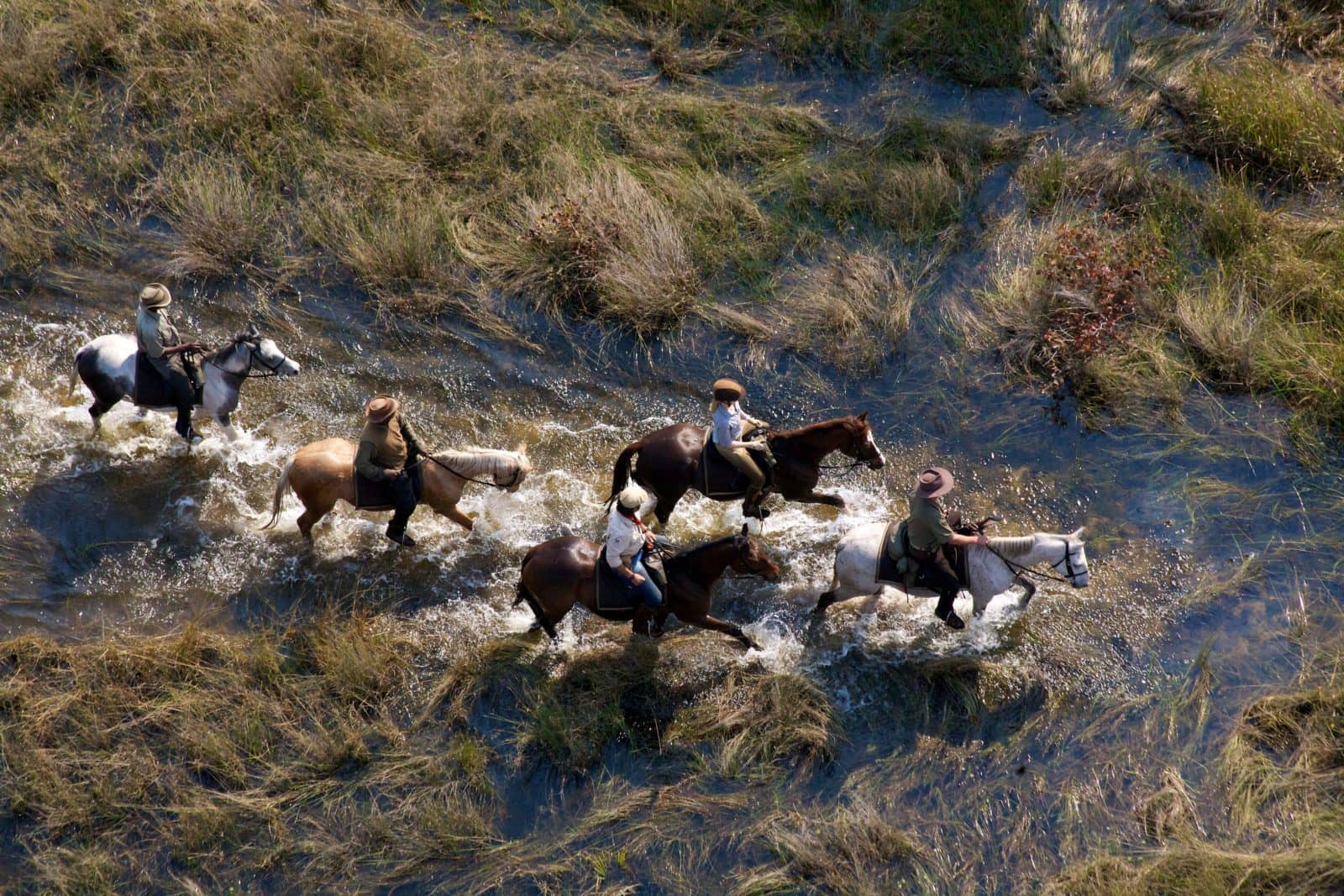 African Horseback Safari rirders splashing through shallow water