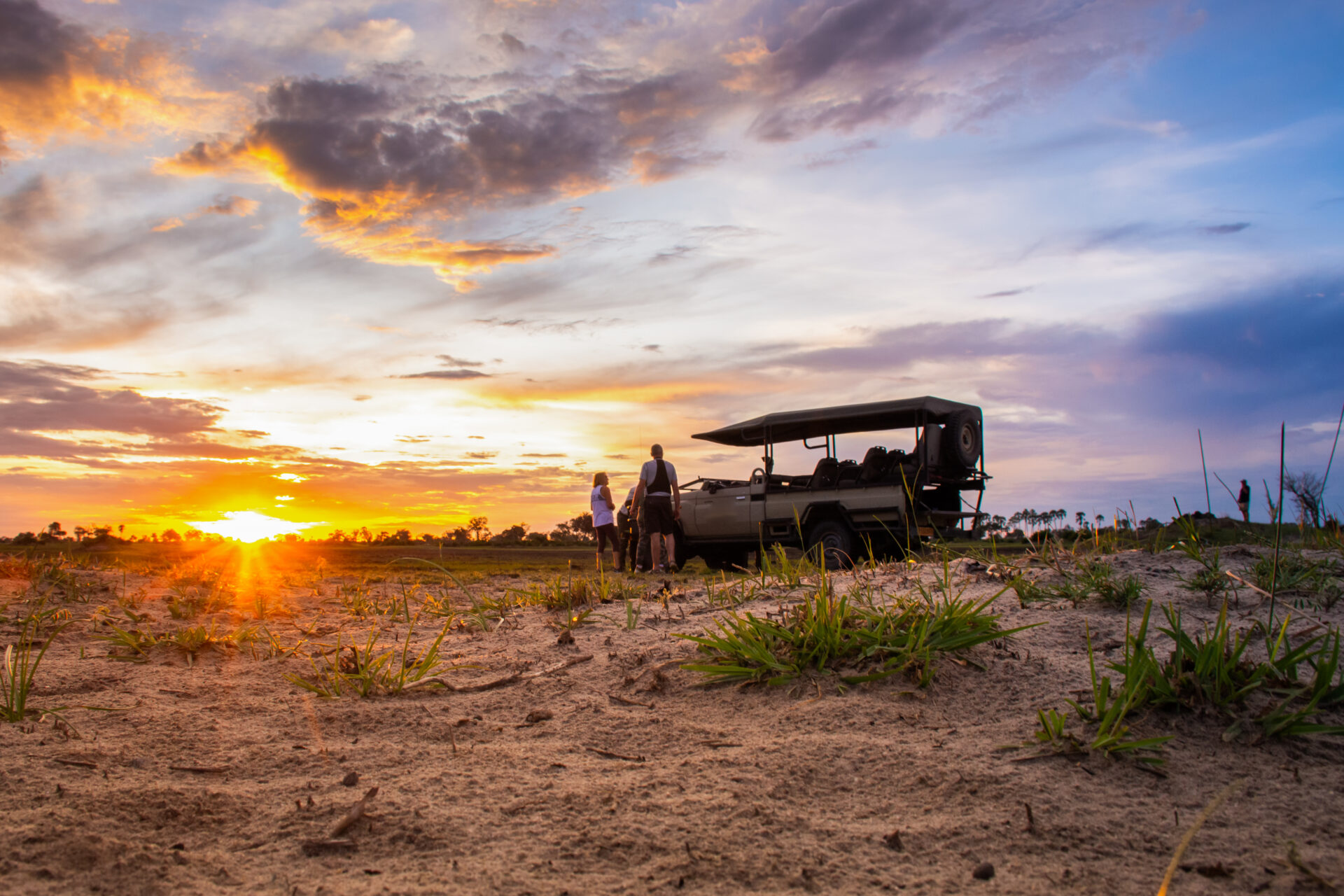 Safari vehicle with guests watching a vibrant sunset over the plains at Pom Pom Camp.