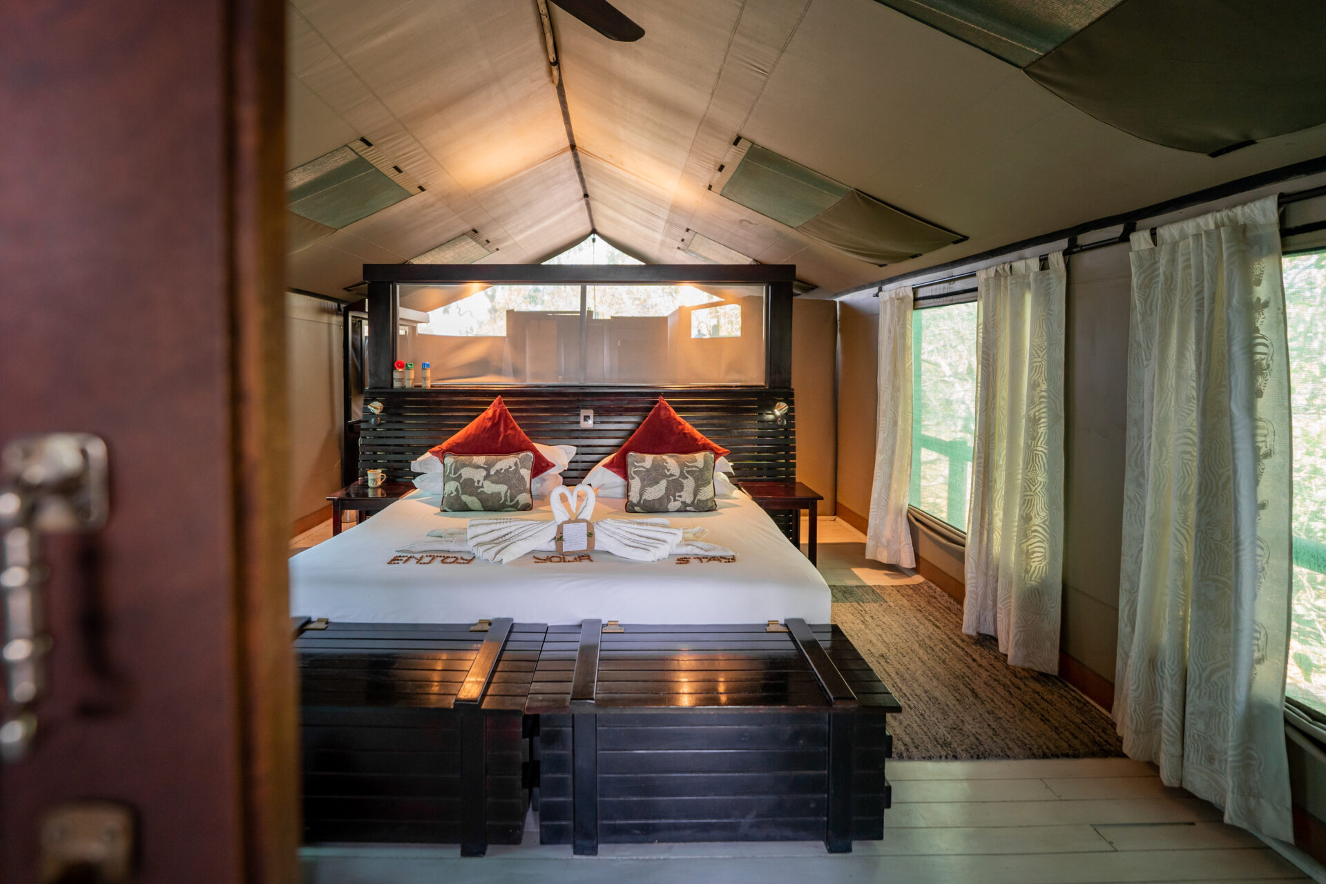 Interior of a luxury safari tent with a king-size bed, red cushions, and natural light at Pom Pom Camp.