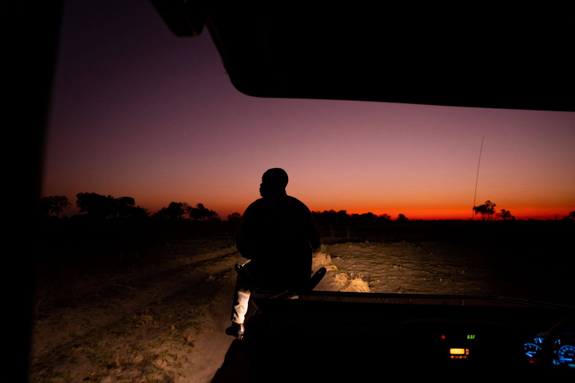 Silhouette of a safari guide seated on a vehicle at dusk during a night game drive at Pom Pom Camp.