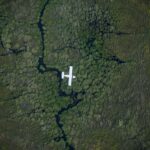 Small airplane flying over waterways and green vegetation in the Okavango Delta.