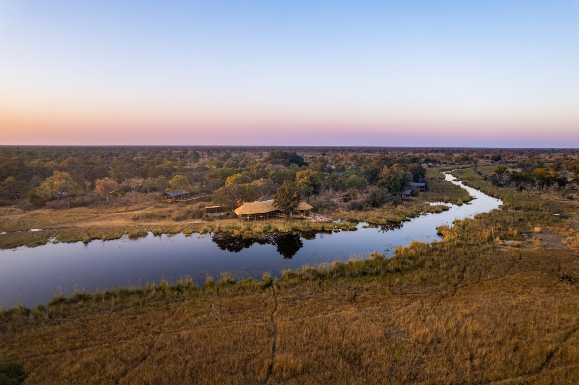 Aerial view of lodge beside river channels at dusk in the Okavango Delta.