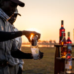 Guide pouring drink at sundowner setup in the Okavango Delta near Four Rivers Camp.