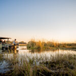 Safari boat with guests gliding through Delta channels at sunset near Four Rivers Camp.