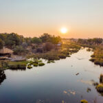Aerial view of Four Rivers Camp beside a winding waterway at sunrise.