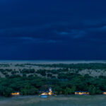 Evening view of guest rooms at King Lewanika Lodge with dramatic stormy skies and lightning in the background