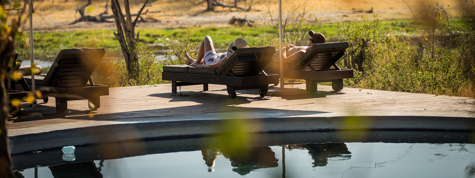 A couple relaxing on sun loungers by the swimming pool overlooking the Okavango flood plains