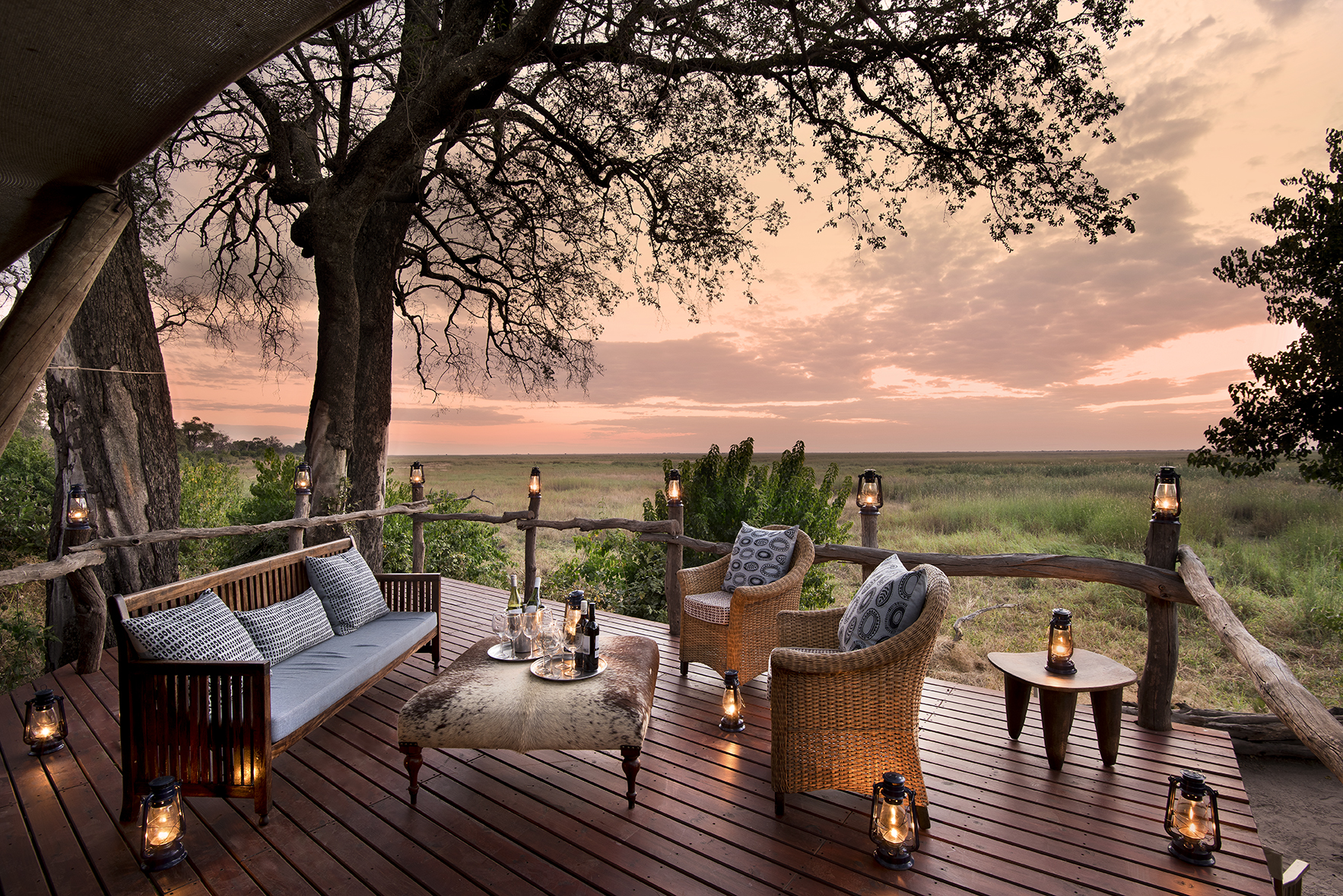 Deck lounge with wicker chairs and lanterns overlooking Linyanti Marsh at sunset in Botswana.