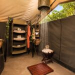 Luxury safari tent bathroom with open-air shower, shelving and traditional safari décor.