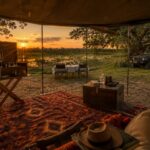The covered safari camp lounge at Harkness Safari private mobile camp, the main area with views across a wetland and sunset beyond.
