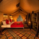 Interior of a luxury Meru safari tent at Harkness safaris with double bed, lanterns, storage shelves and patterned rugs.