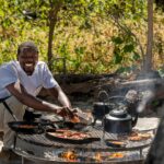 Chef preparing breakfast over open fire at Nxabega Under Canvas boma in the Okavango Delta