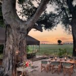 Boma dining and sundowner bar setup at Nxabega Under Canvas with lanterns and Delta views at sunset