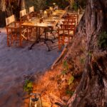 Boma evening dining setup at Nxabega Under Canvas with lantern-lit table under trees in the Okavango Delta